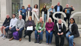 A group of health and safety reps smiling for the camera, in front of the UNISON sign