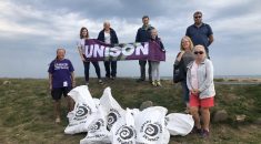 UNISON members take part in beach clean in Devon. Several members stand on a beach holding a UNISON flag showing the rubbish they collected.