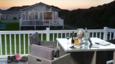 Sunset over a lodge at Croyde Bay where a table hosts a glass of wine and shoes from a busy day are strewn across the decking.