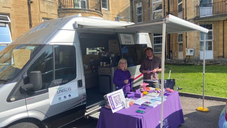 UNISON staff are all smiles outside Bath Royal United Hospital. The sun is shining and there's a van parked with a table in front covered with a UNISON tablecloth.