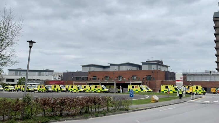 A queue of ambulances outside a hospital in the South West on a cloudy day.