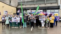 Health care staff brave the rain with umbrellas outside Derriford Hospital. They hold Put NHS Pay Right signs.