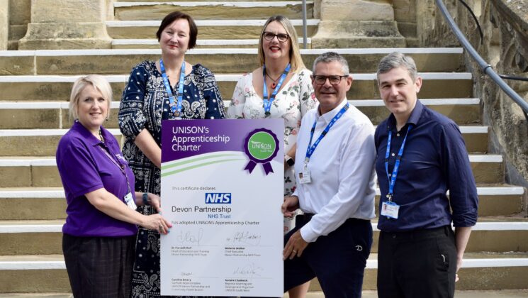 Signatories of UNISON's Apprenticeship Charter at Devon Partnership NHS Trust stand holding an oversized certificate outside Wonford House in Exeter.