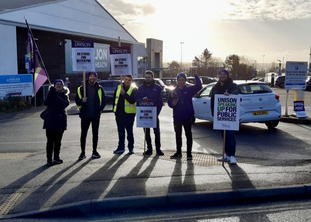 UNISON members on the picket line with low winter sun behind them casting long shadows on the ground.