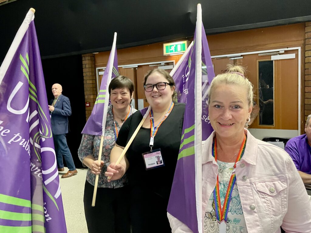 Rhian, Julia and Lorraine walk into national delegate conference holding UNISON flags.