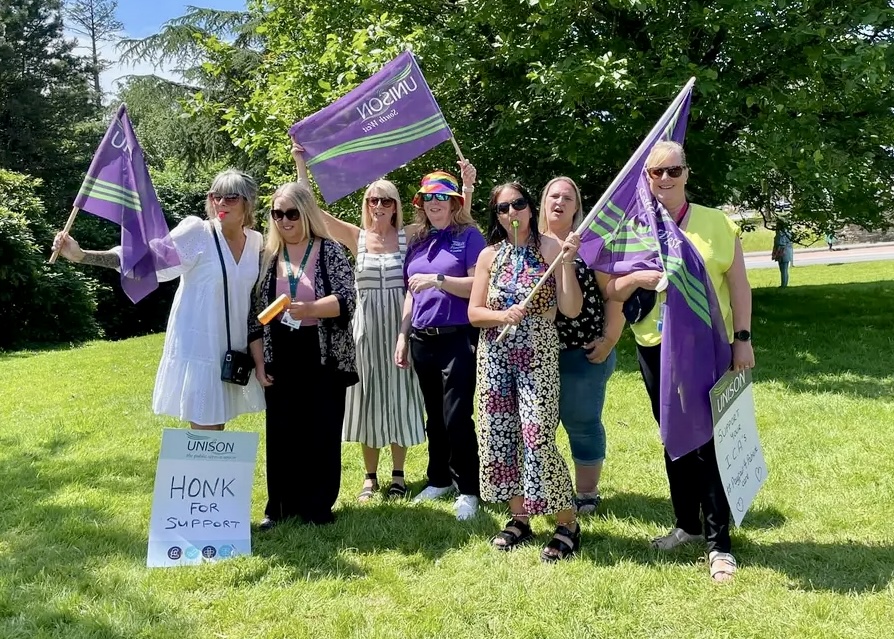 UNISON members hold purple UNISON flags on the picket line in Plymouth.